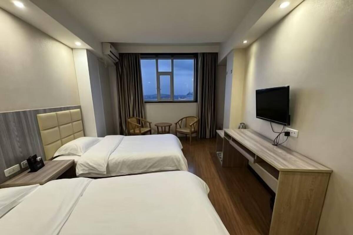 Ein Hotelzimmer mit zwei Betten, einem Fernseher, einem kleinen Tisch und einem Fenster mit Vorhängen.