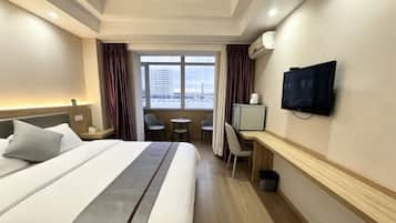 Ein Hotelzimmer mit Bett, Schreibtisch, Fernseher und Blick auf die Stadtlandschaft durch das Fenster.