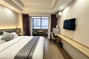 A hotel room with a bed, a desk, a television, and a view of the cityscape through the window. - Laiyinhe Fashion Motel (Hunchun)