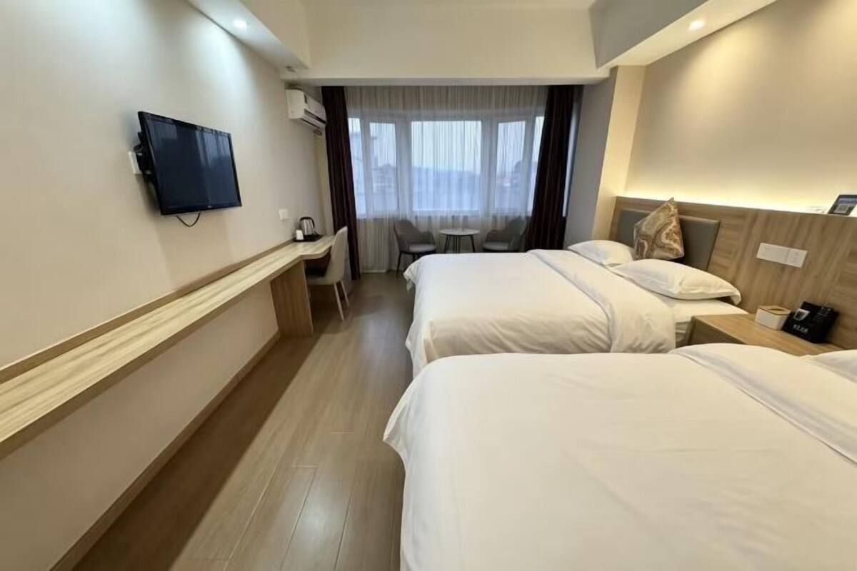 Ein Hotelzimmer mit zwei Betten, einem Schreibtisch, einem Fernseher und einem Fenster mit Vorhängen.