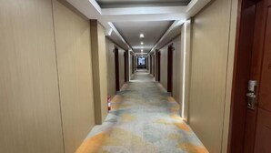 A hotel corridor with a patterned carpet, wooden doors, and recessed lighting.