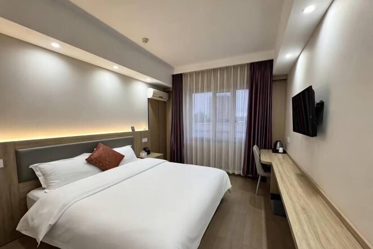 Ein Hotelzimmer mit einem Bett, einem Schreibtisch, einem Fernseher und einem Fenster mit Vorhängen.