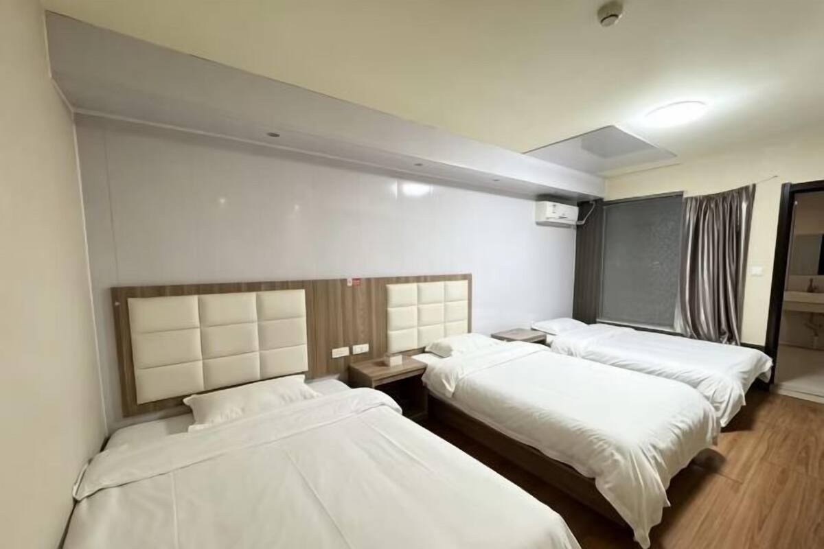Ein Hotelzimmer mit zwei Betten, einem hölzernen Kopfteil, einem Nachttisch und einem Fenster mit Vorhängen.
