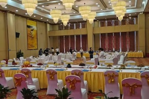 Un salón de banquetes con mesas redondas, sillas y una zona de escenario.