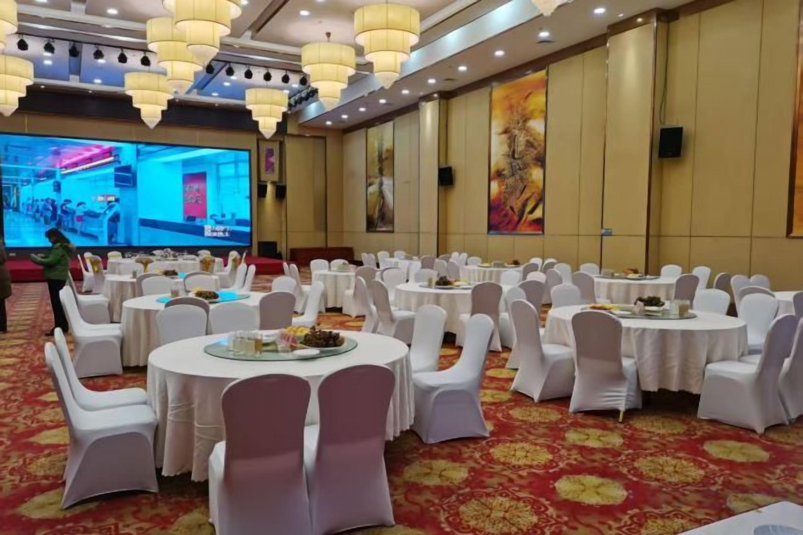 A banquet hall with round tables, white chairs, and a large screen for presentations.