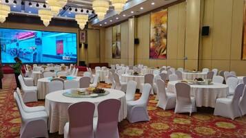 A banquet hall with round tables, white chairs, and a large screen for presentations.