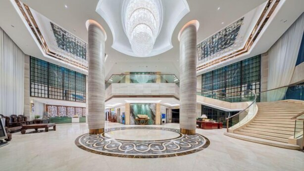 A spacious lobby with a central circular design, a grand chandelier, and a staircase leading to upper floors.