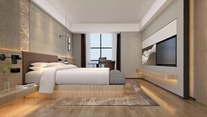 A modern bedroom with a large bed, a TV mounted on the wall, and a small table with a chair in the background.