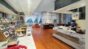 A modern hotel lobby with a marble reception desk, a dining area with a buffet, and a large window offering a view.