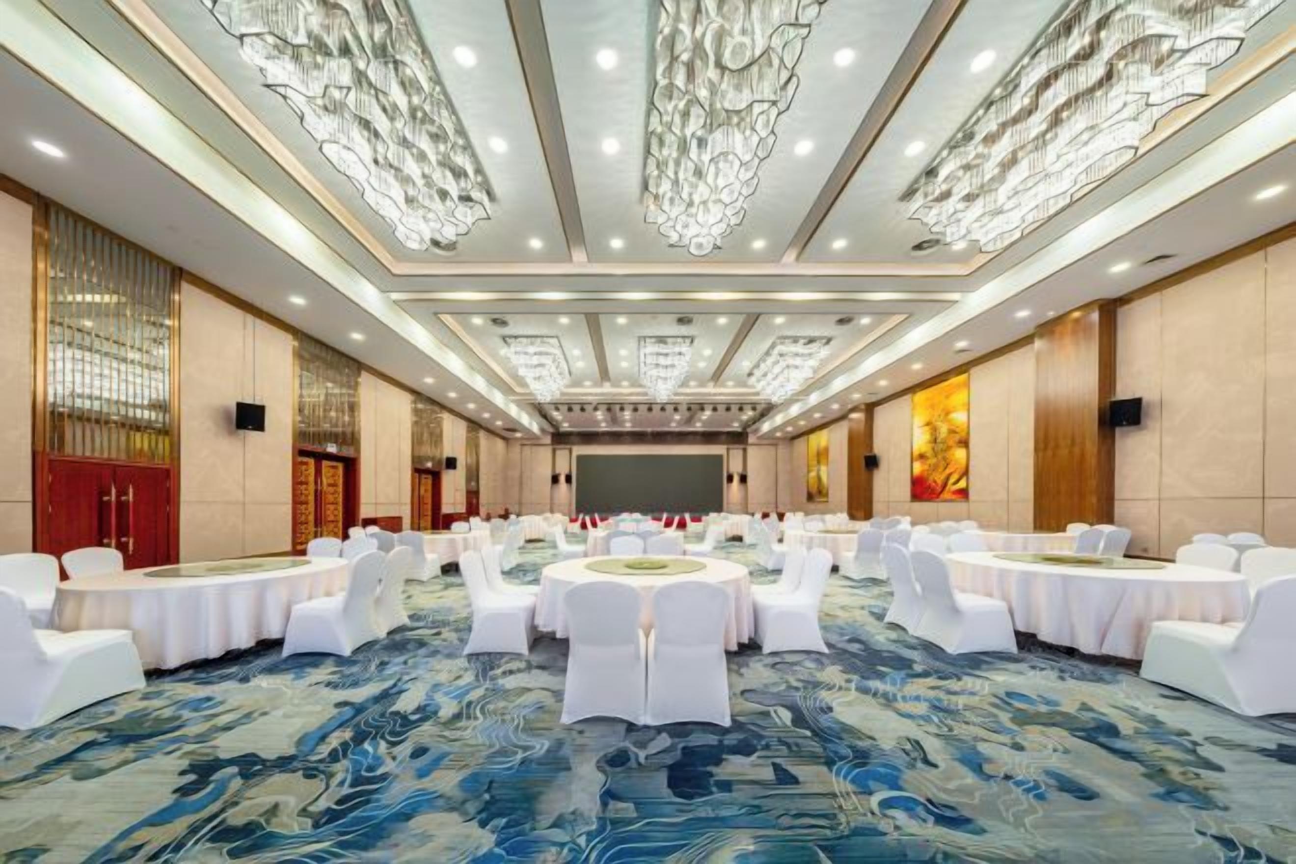 A conference room with round tables, white chairs, and a blue patterned carpet.