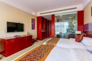 A hotel room with a TV, a red cabinet, a bed with a patterned bed runner, and a glass door leading to a bathroom. - Jinhua Kokusai Hotel (Pingxiang)