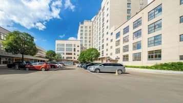 A parking lot with several cars, a building with multiple floors and large windows, and a clear blue sky.