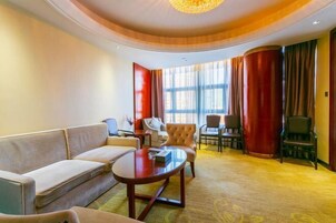 A hotel room with a sofa, a round table, and a chair. There is a window with curtains and a view of the outside.