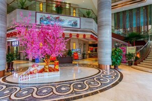 A spacious lobby with a central decorative tree, a staircase, and a large painting on the upper level.