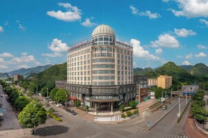 Un gran hotel de varios pisos con una cúpula central y una distribución circular, rodeado de vegetación y montañas.