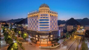 A multi-story hotel with a central dome and a modern facade, surrounded by a landscaped area and a busy street.