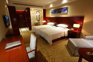 A hotel room with two beds, a desk, a chair, a small table, and a shower area.
