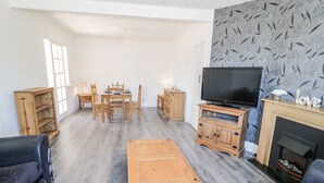 Een woonkamer met een houten salontafel, een televisie op een meubel, een open haard en bloemenbehang.