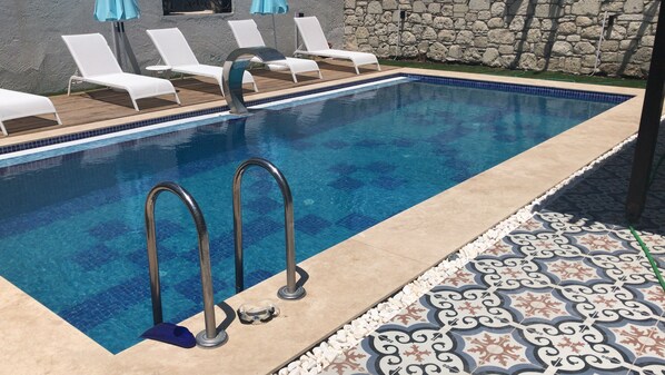 Ein Pool mit gefliestem Rand, einer Steinmauer und einer Liegefläche mit Liegestühlen.