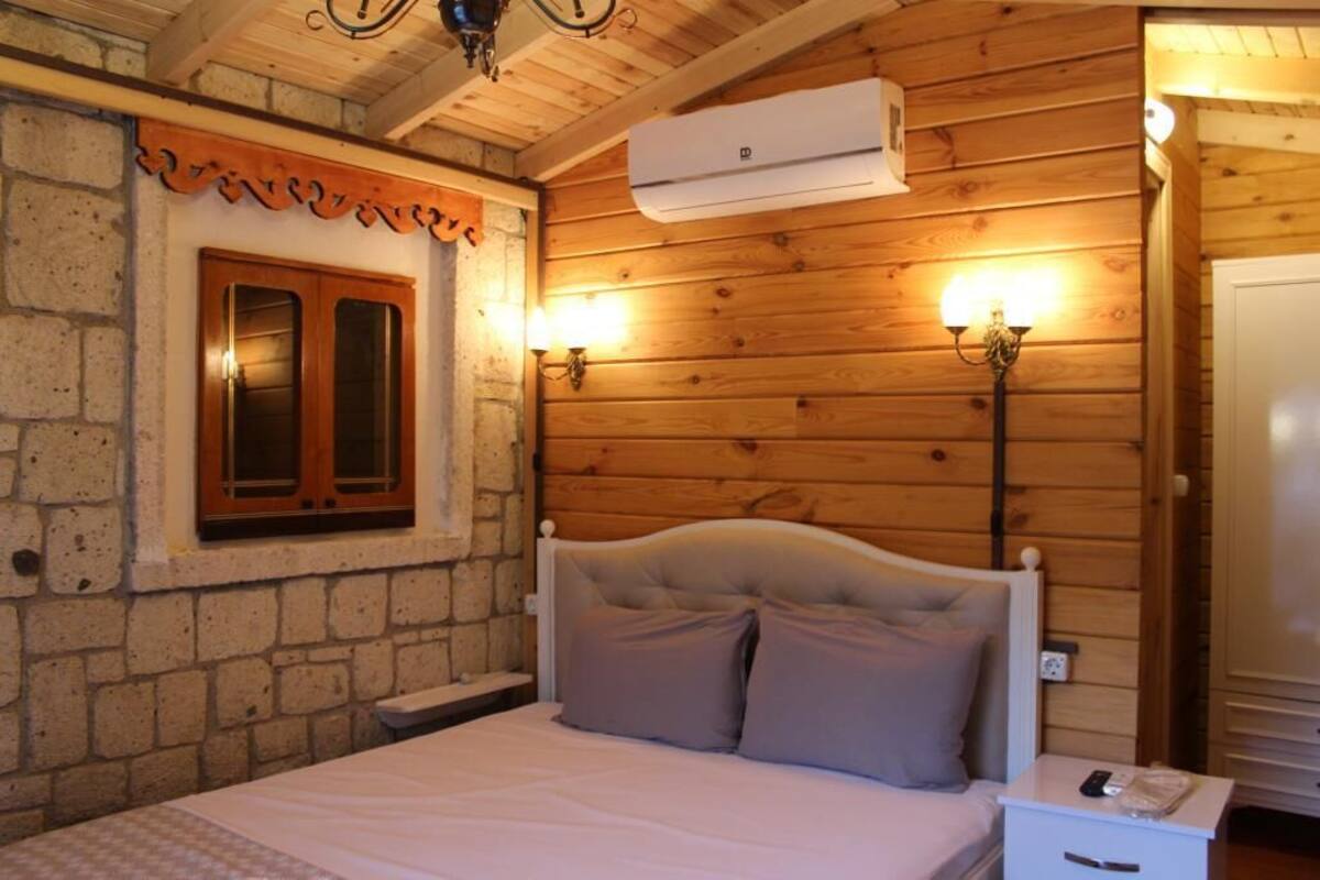 A wooden-paneled room with a bed, a stone wall, a window with wooden shutters, and a wall-mounted air conditioner.