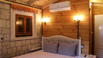 Una habitación con paneles de madera, una cama, una pared de piedra, una ventana con contraventanas de madera y un aire acondicionado instalado en la pared.