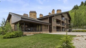 Un bâtiment moderne à plusieurs étages, doté d’une façade en pierre, d’un espace extérieur couvert et d’une pelouse bien entretenue.