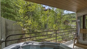 Un bain à remous sous une pergola en bois, avec vue sur une zone boisée.