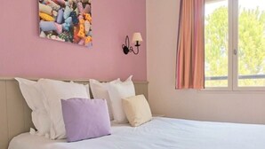 A bedroom with a bed, pillows, a wall-mounted lamp, and a window with curtains. - 45 m2 house, facing the pine forest, terrace, garden and tranquillity (Mallemort)