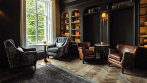Une bibliothèque avec des étagères en bois foncé, des fauteuils en cuir et une grande fenêtre donnant sur les arbres.