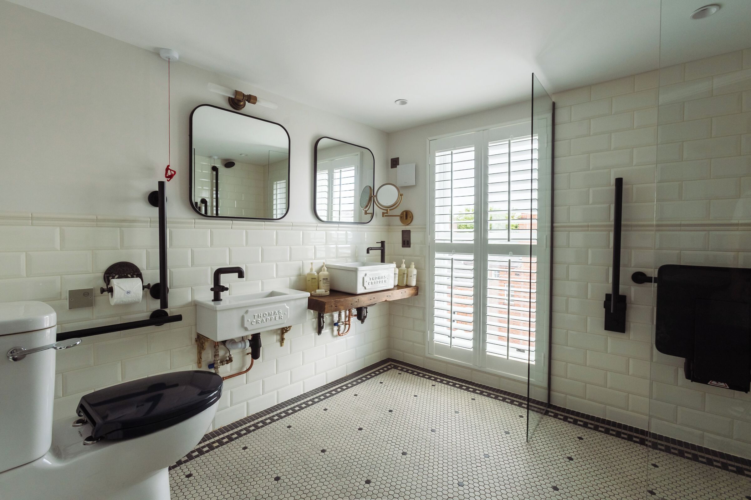 A bathroom with a toilet, sink, and mirrors. There is a window with blinds and a towel rack.