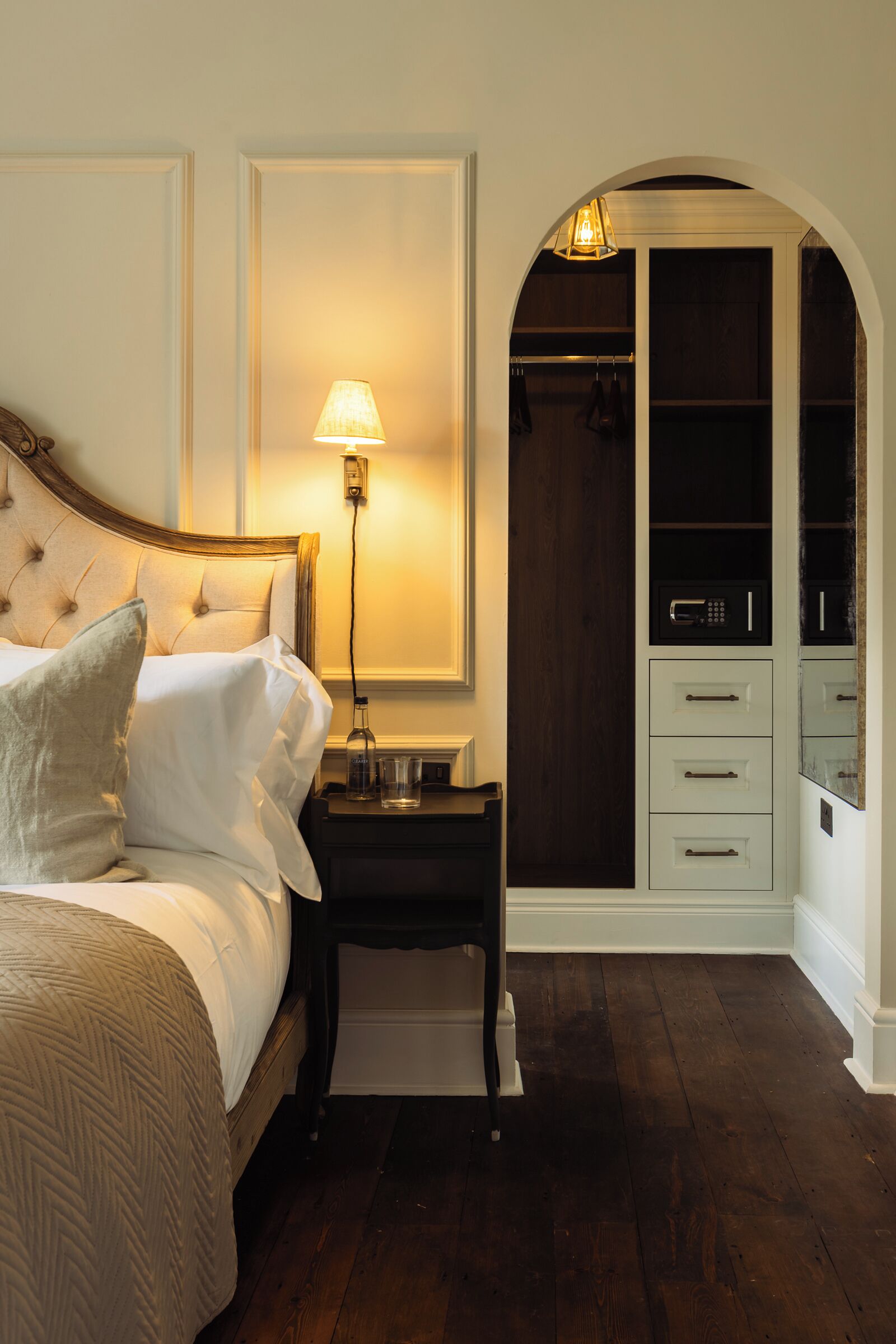 Een slaapkamer met een bed, bedlamp, nachtkastje en een inloopkast met lades en planken.