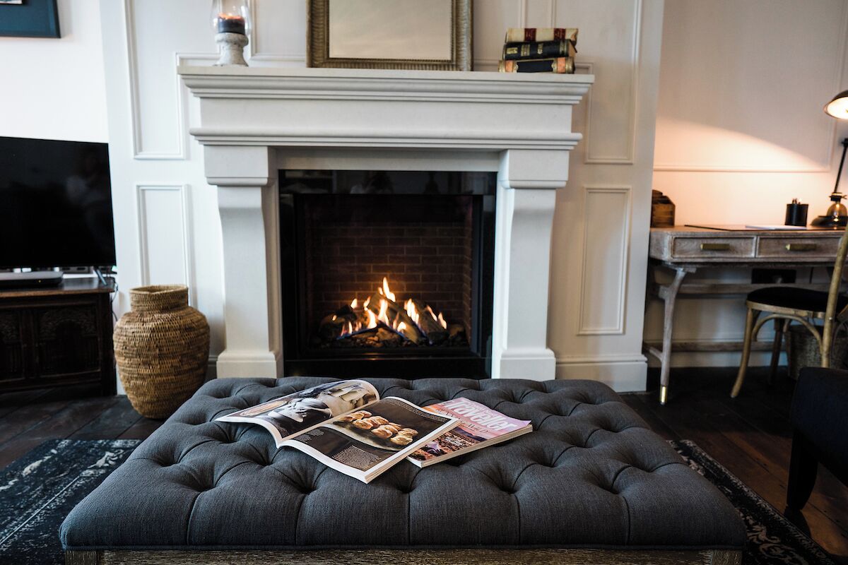 Un salon chaleureux avec une cheminée, un pouf capitonné agrémenté de magazines, un téléviseur et un bureau avec une lampe.