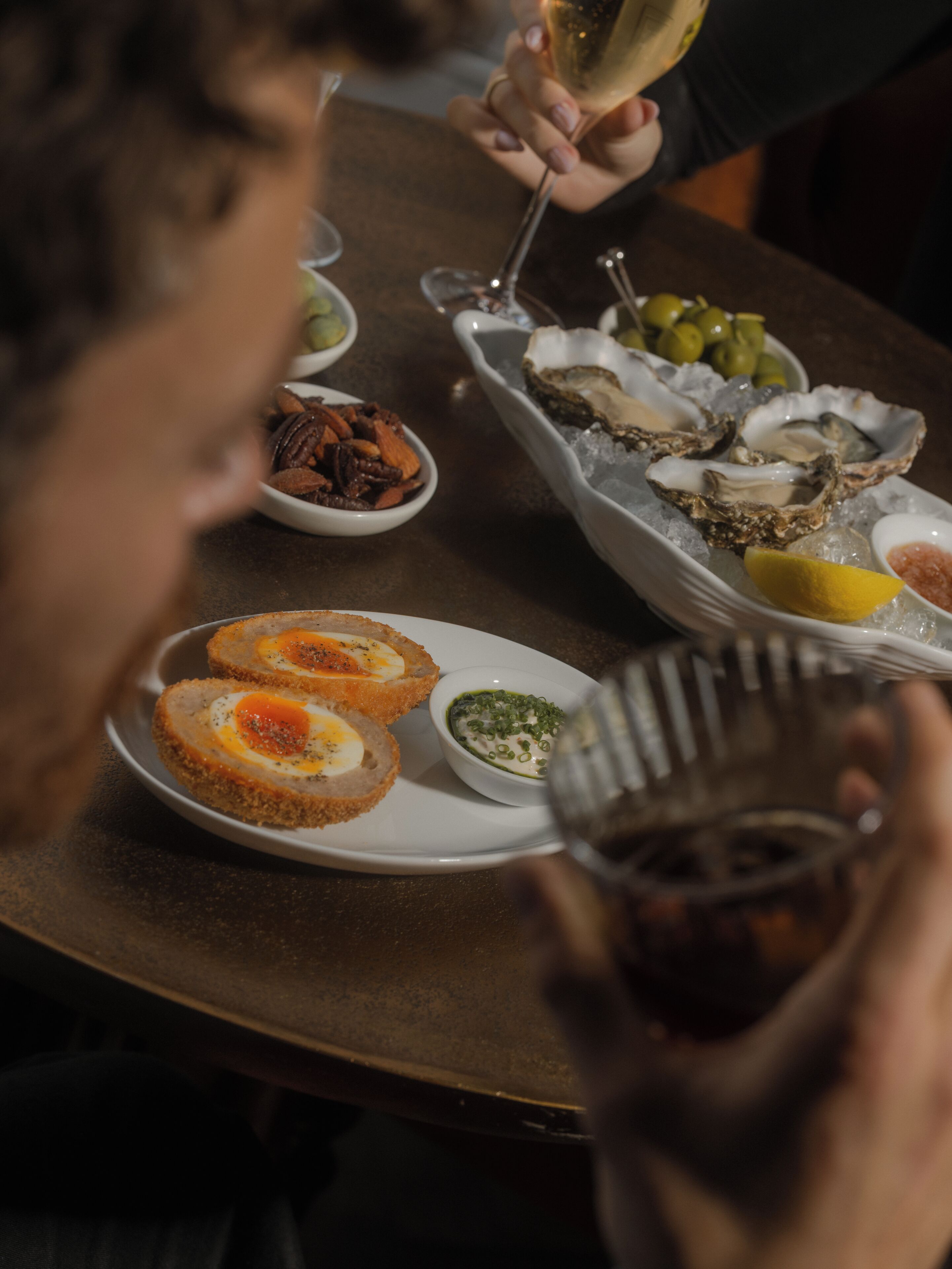Een eettafel met zeevruchten, een glas wijn, en een persoon die een glas vasthoudt.