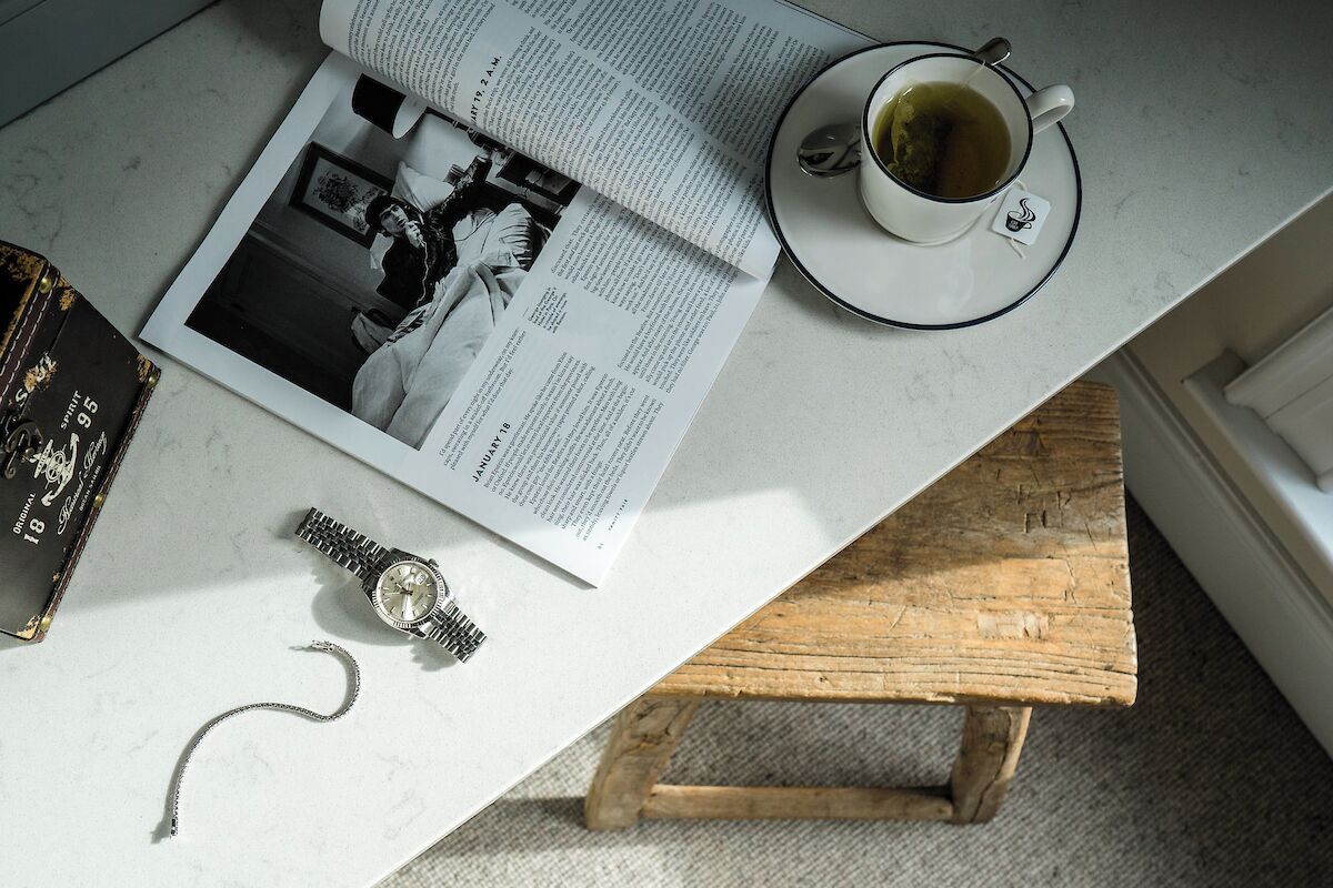 A table with a book, a cup of tea, a watch, and a bracelet.