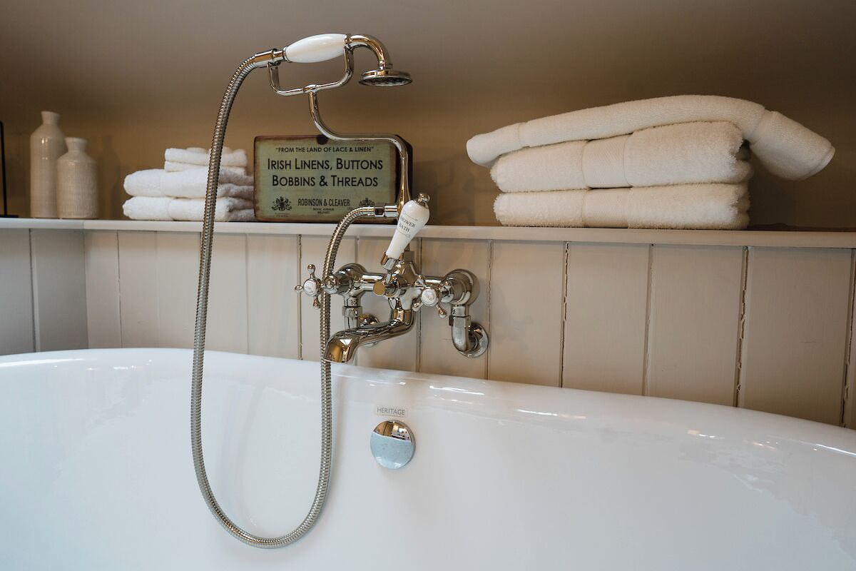 Eine Vintage-Badewanne mit Duschkopf, umgeben von ordentlich gestapelten weißen Handtüchern und einem Schild, das IRISH LINENS, BUTTONS und THREADS anwirbt.