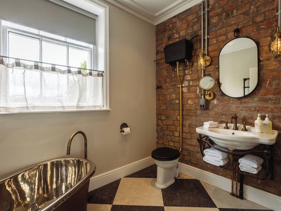 Une salle de bain avec une baignoire sur pieds, des toilettes, un lavabo avec un miroir et un mur en briques.