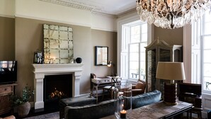 Un salon chaleureux avec une cheminée, des fauteuils confortables et un lustre.