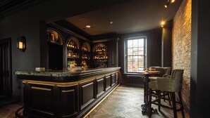 Un espace bar avec un comptoir en bois foncé, des étagères remplies de bouteilles et un mur en briques.