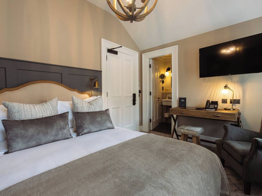 A hotel room with a large bed, a desk with a chair, a television mounted on the wall, and a door leading to a bathroom.