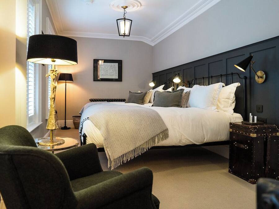 A bedroom with a large bed, a dark headboard, a floor lamp, a side table, and a suitcase.