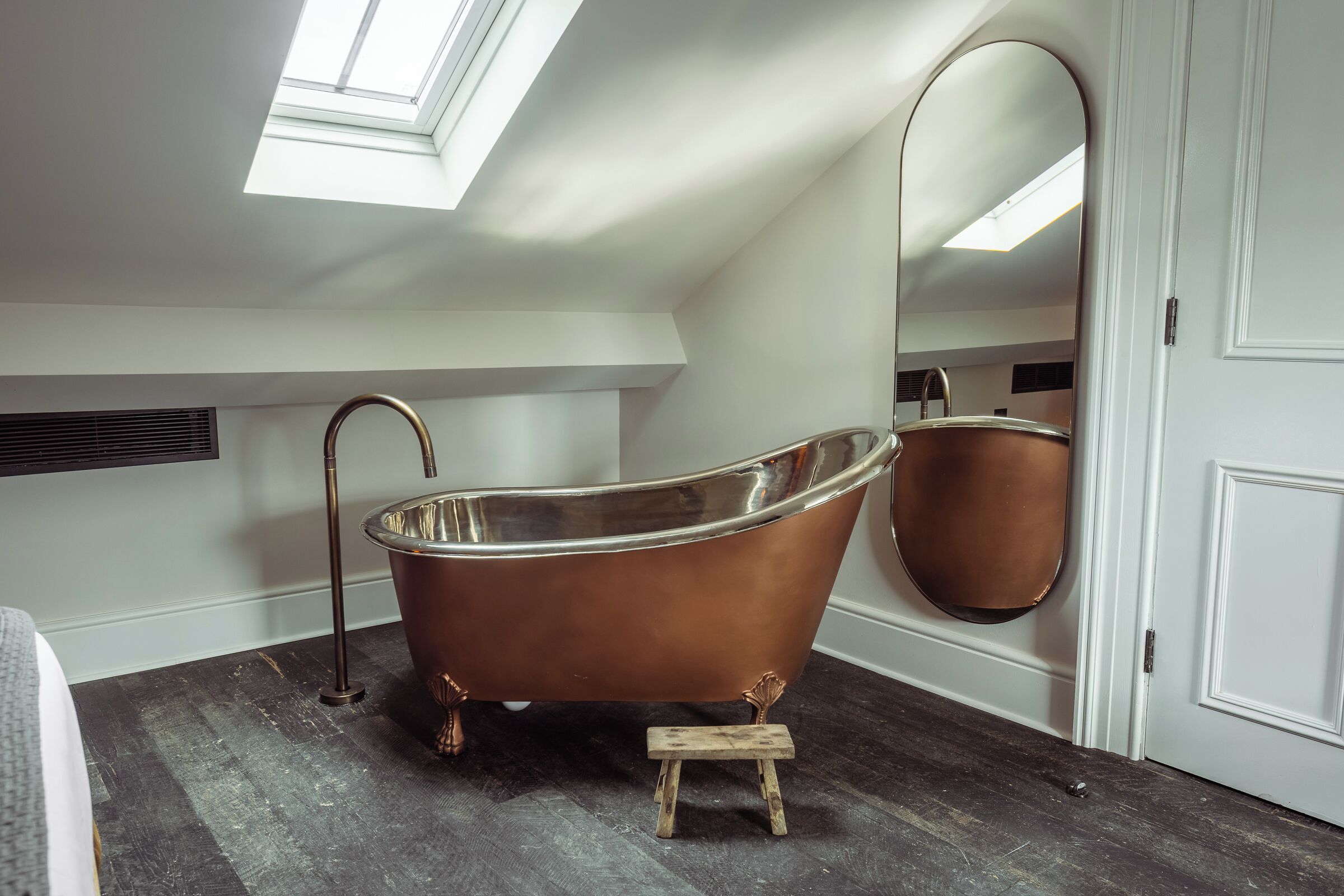 A modern bathroom with a freestanding copper bathtub, a skylight, and a large mirror.