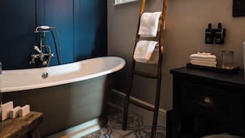 A bathroom with a freestanding bathtub, a wooden ladder, a vanity with a mirror, and a window.