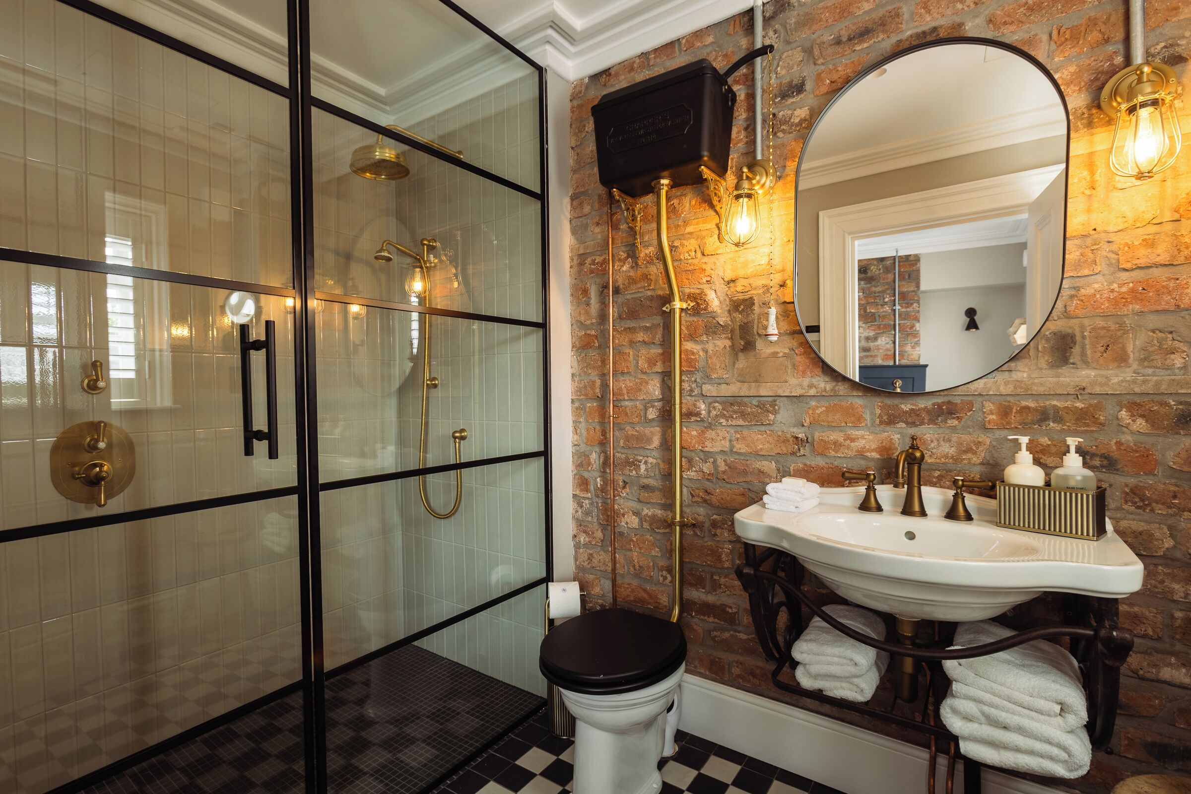 A bathroom with a glass-enclosed shower, a white sink with gold fixtures, and a large mirror.