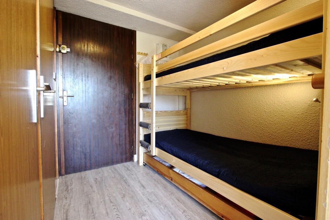 Una habitación pequeña con una litera, un armario de madera y una puerta.