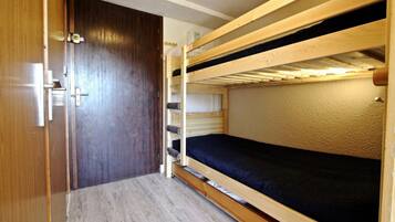 Una habitación pequeña con una litera, un armario de madera y una puerta.