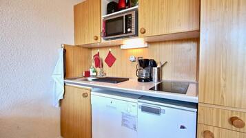 Cocina compacta con armarios de madera, microondas, cafetera y lavavajillas.