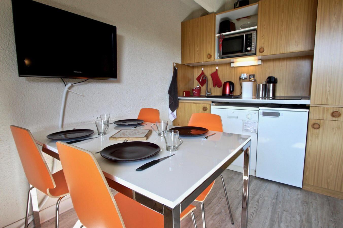 A compact kitchen with a microwave, toaster, and small refrigerator. A dining table with chairs is set for two.
