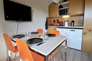 A compact kitchen with a microwave, toaster, and small refrigerator. A dining table with chairs is set for two.