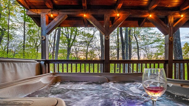 Ein Whirlpool mit einem Glas Rotwein, umgeben von einer Holzterrasse und Bäumen.