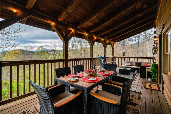 A covered outdoor dining area with a wooden deck, wicker chairs, and a table set for four.